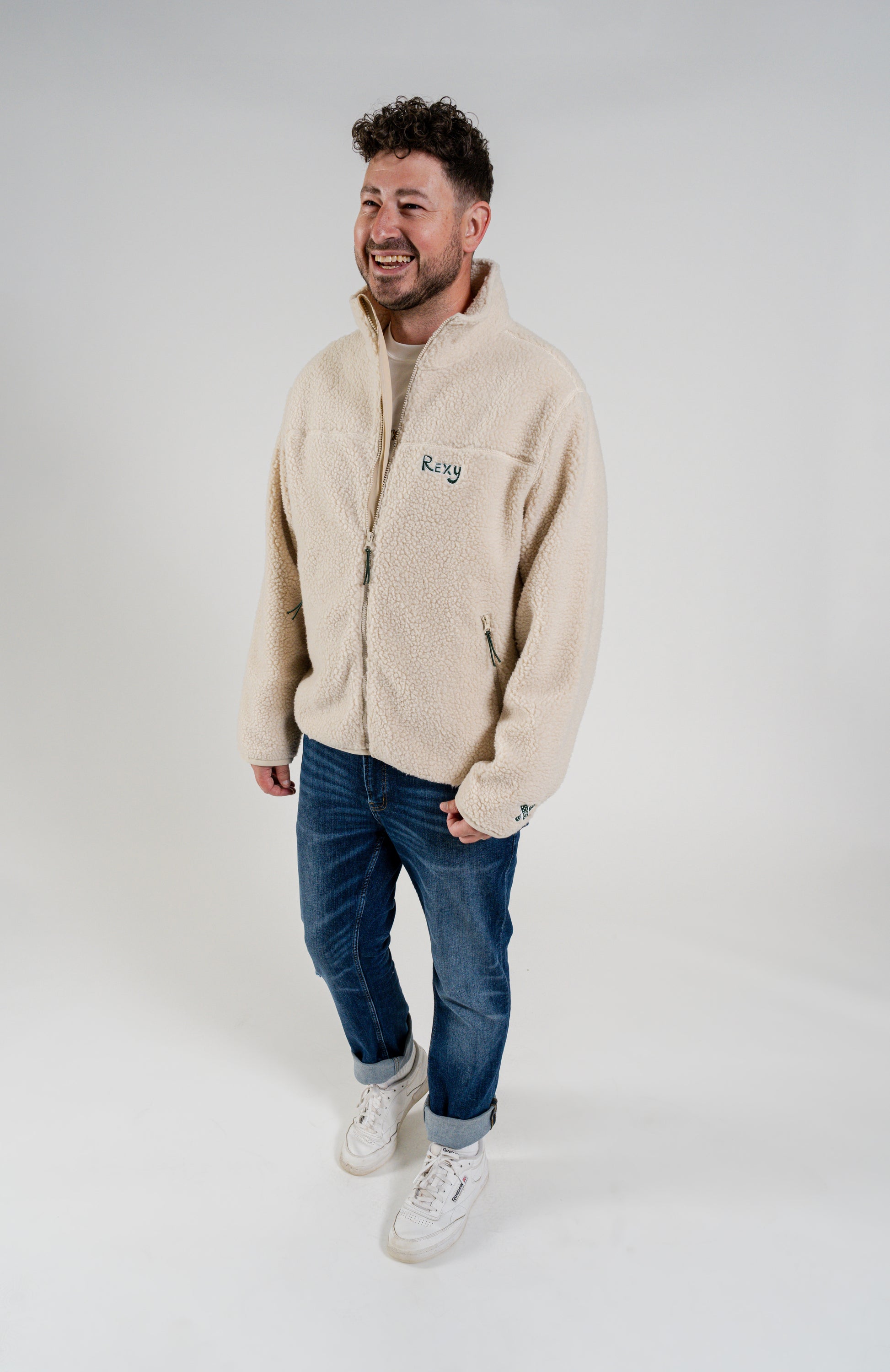 man standing wearing a cream sherpa jacket with rexy embroidery